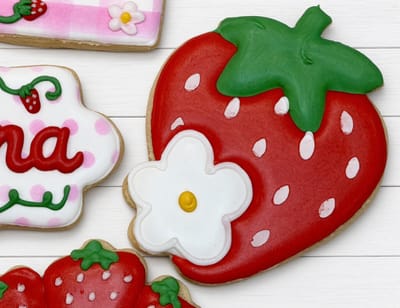 Bright red strawberry cookie with a white daisy and trailing vines — custom decorated cookies by Dreams of Buttercream